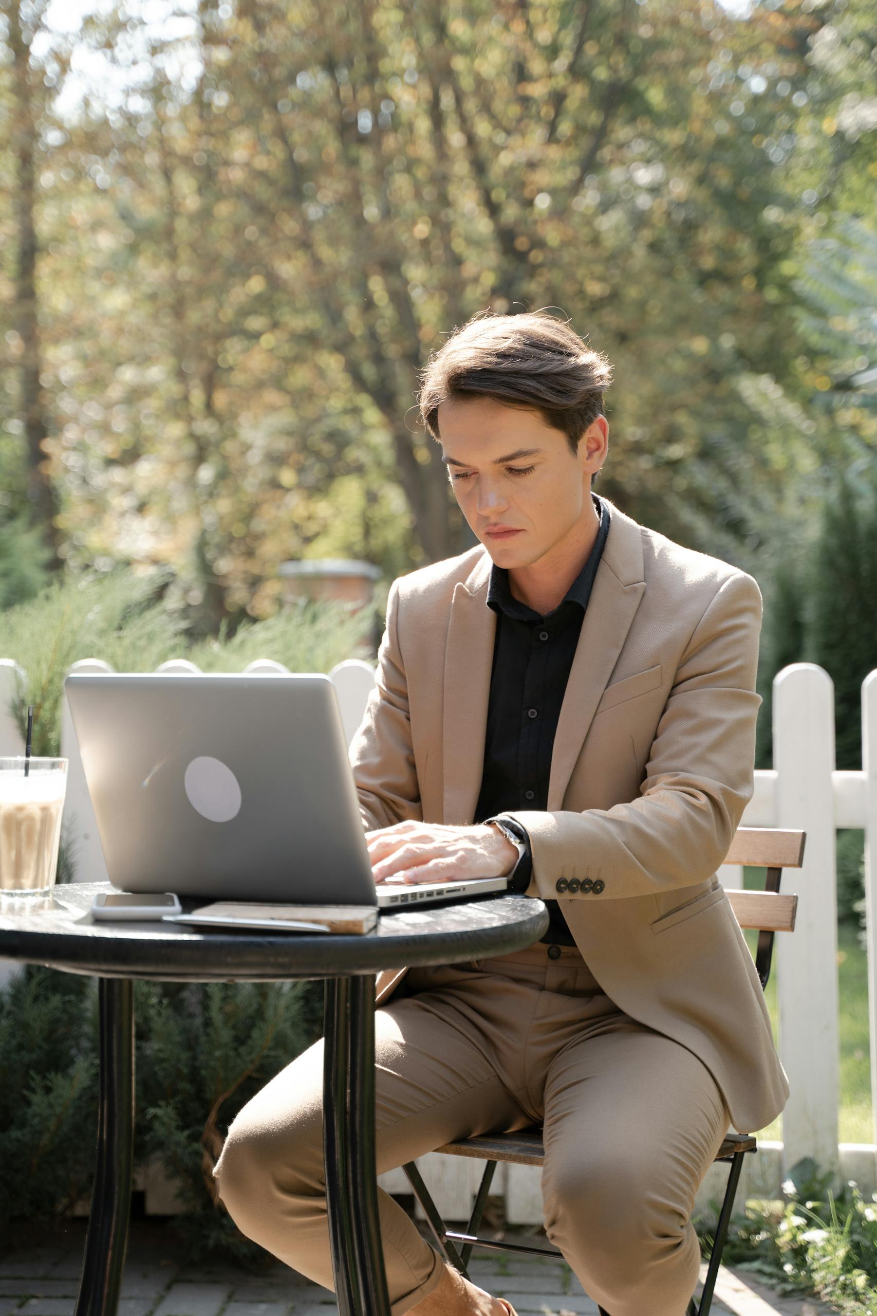 Professional young man in beige suit working on laptop outdoors.